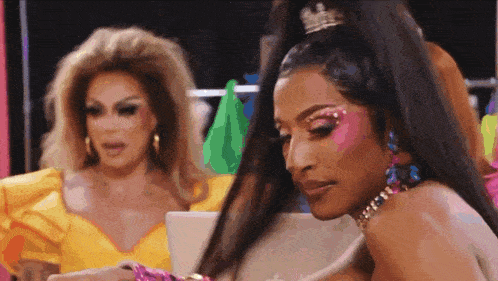 two drag queens are standing next to each other and one of them is wearing a yellow dress .