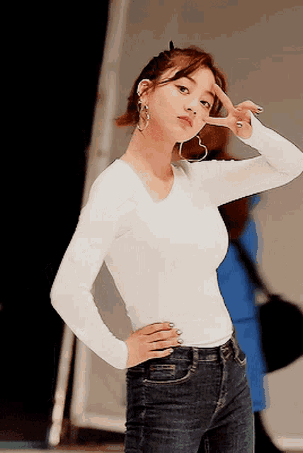 a woman wearing a white shirt and blue jeans is giving a peace sign