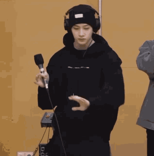 a young man wearing headphones and a beanie is holding a microphone and dancing .