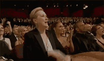 a woman in a tuxedo is sitting in a crowd of people applauding at an awards show .