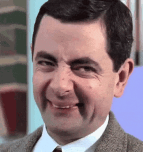 mr bean is wearing a suit and tie and smiling .