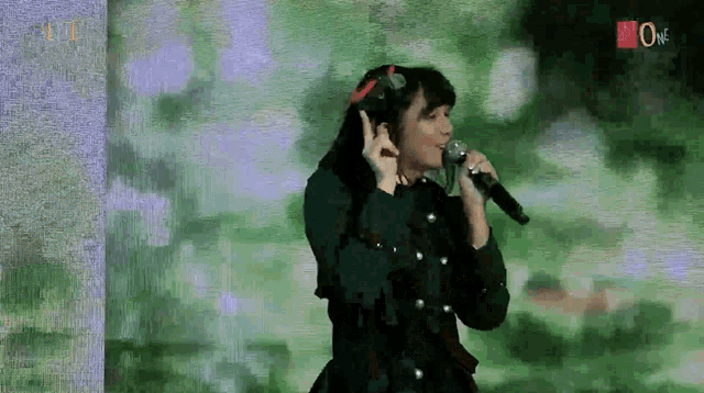 a woman is singing into a microphone in front of a green screen .