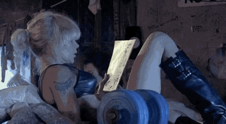 a woman is reading a book while laying on a bed next to a dumbbell .