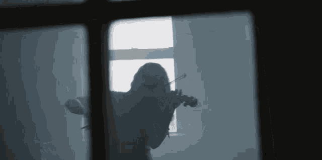 a woman is playing a violin in front of a window in a dark room