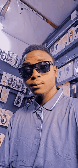 a man wearing sunglasses and a blue shirt is standing in front of a shelf full of headphones