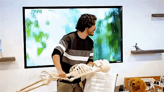 a man standing next to a skeleton in front of a large screen .