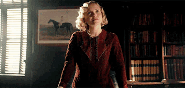 a woman in a red dress is standing in front of a bookshelf with a picture of horses on it