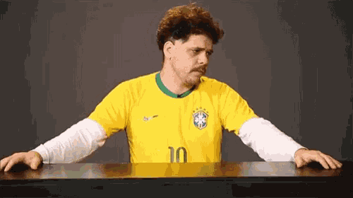a man wearing a yellow soccer jersey with the number 10 on it is sitting at a table .