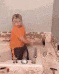 a young boy in an orange shirt is holding a hammer while standing next to a sink .