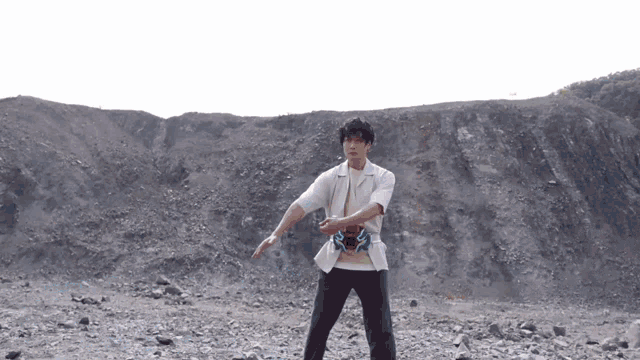 a man in a white shirt is standing in a rocky area with his arms outstretched .