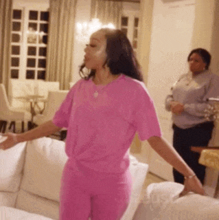 a woman in a pink outfit is standing in a living room with her arms outstretched .