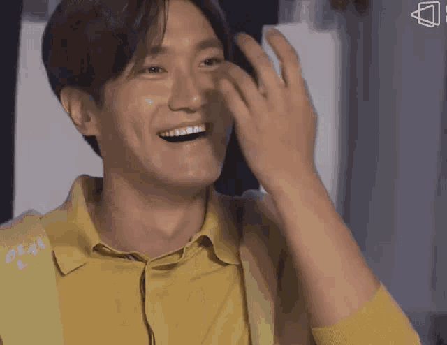 a man in a yellow shirt is laughing and covering his face with his hand .