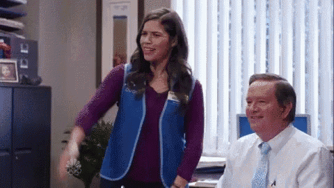 a woman in a blue vest is standing next to a man in a suit and tie in an office .
