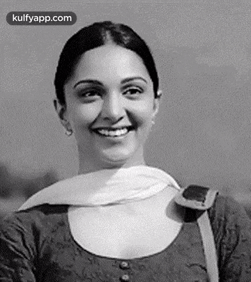 a black and white photo of a woman smiling and looking at the camera .