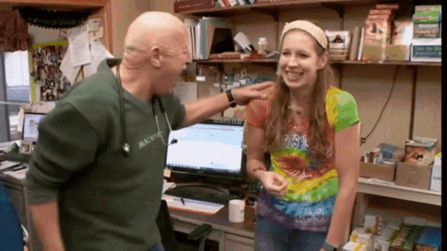 a man wearing a green shirt that says mackenzie is talking to a woman in a tie dye shirt