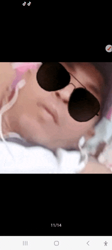 a man wearing sunglasses and a hat is laying down on a bed .
