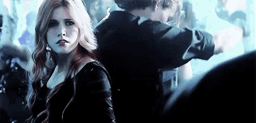 a woman in a black dress is standing in a crowd of people in a dark room .