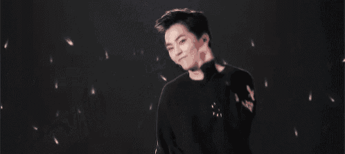 a young man in a black sweater is dancing on a stage with his hands in the air .