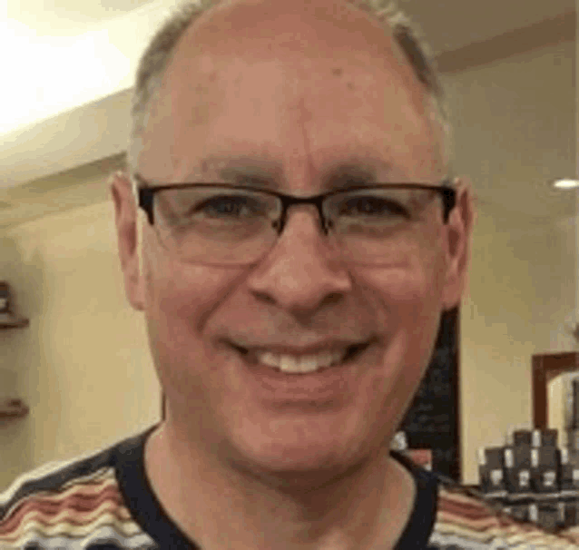 a close up of a man wearing glasses and a striped shirt smiling .