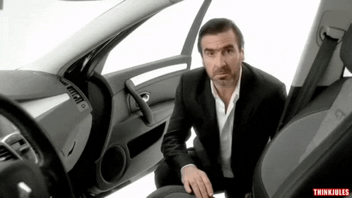 a man in a suit sits in the driver 's seat of a car with thinkjules written on the bottom right