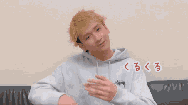 a man wearing a gray stussy hoodie sitting on a couch