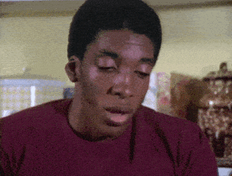 a man in a red shirt is sitting in a kitchen with his mouth open .