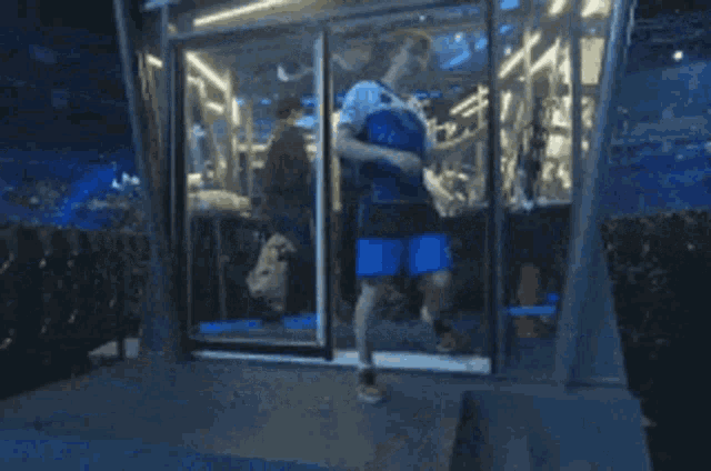 a man in a blue shirt and shorts is walking through a glass door