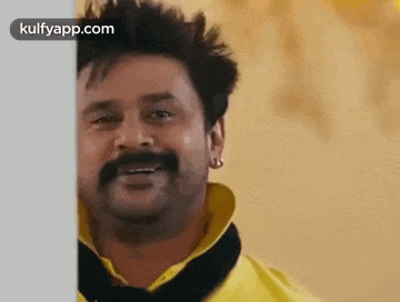 a man with a mustache is standing behind a wall .