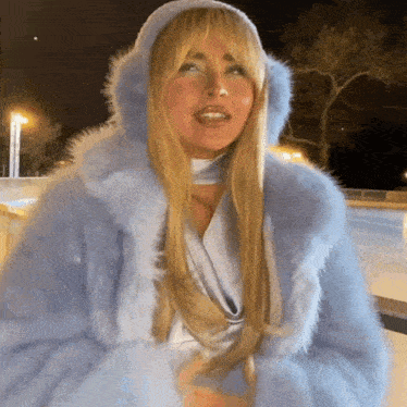 a woman wearing a blue fur coat with a hood is standing on a ice rink .
