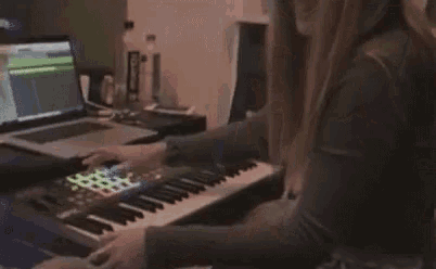 a woman is sitting at a desk playing a keyboard with a laptop .