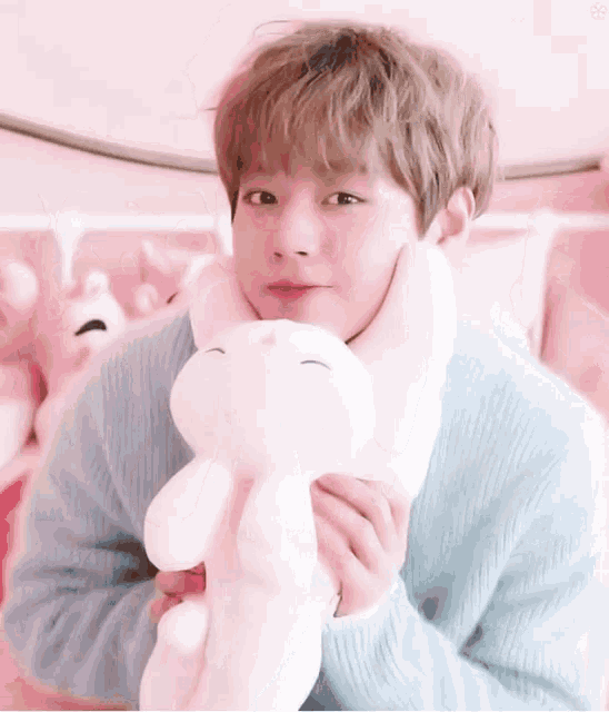 a young boy in a blue sweater is holding a pink stuffed animal