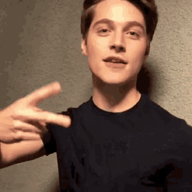a young man is making a peace sign with his hands while wearing a black shirt .