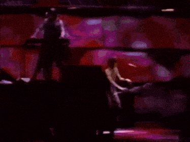 a man is playing a keyboard in front of a microphone in a dark room