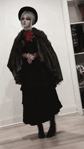 a woman in a black dress and cape is standing in front of a white wall