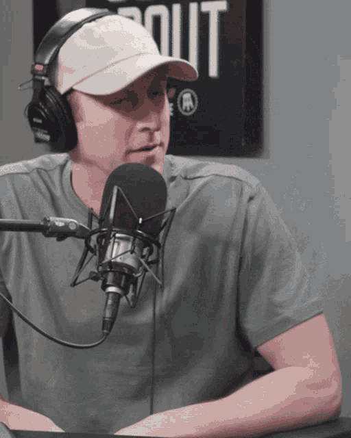 a man wearing headphones and a hat talks into a microphone in front of a sign that says out