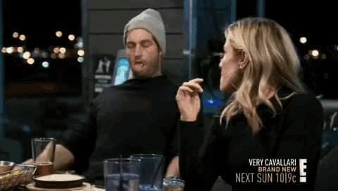 a man and a woman are sitting at a table in front of a sign that says very cavallari
