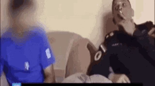 a man is smoking a cigarette while sitting on a couch with another person .