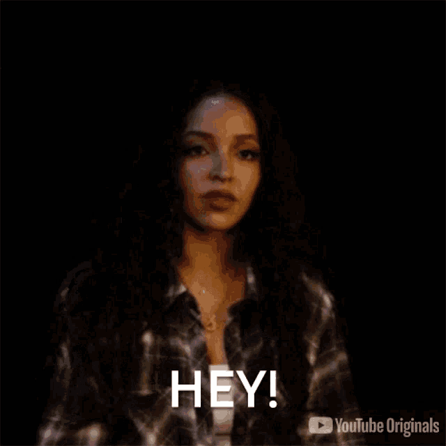 a woman in a plaid shirt is saying `` hey '' in a dark room .