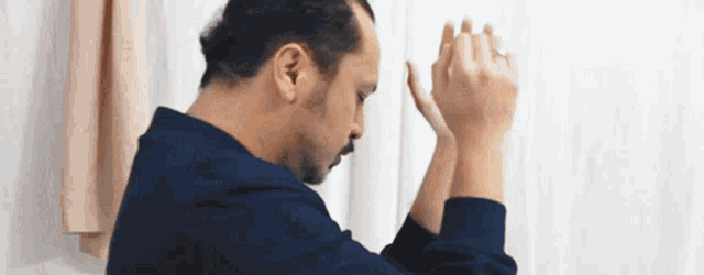 a man with a beard is praying with his hands folded in front of a window .