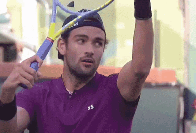 a man in a purple shirt holds a tennis racquet over his head