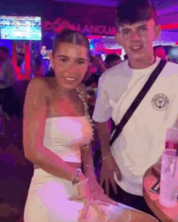 a man and a woman are posing for a picture in a bar . the woman is wearing a white strapless top .