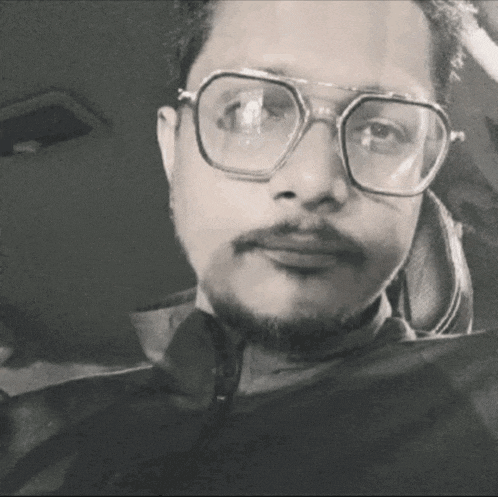 a man with glasses and a beard looks at the camera in a black and white photo