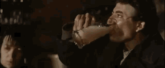 a man is drinking from a bottle in a dark room while a woman watches .