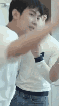 a man in a white shirt and blue jeans is standing in front of a mirror with his arms outstretched .