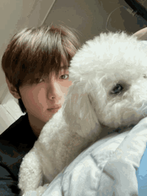 a young man is laying on a bed with a small white dog next to him