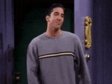 a man in a grey sweater is smiling in front of a purple door