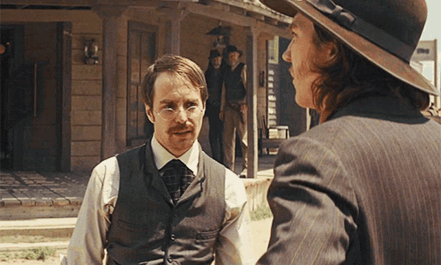 a man in a suit talks to another man in a cowboy hat