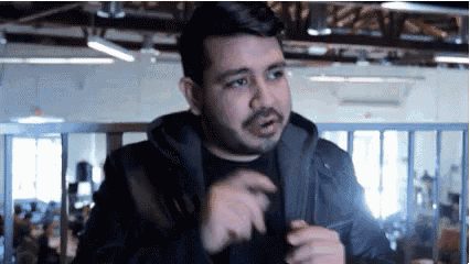 a man with a beard is wearing a black jacket and a black shirt and is standing in a room .