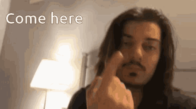 a man with long hair and a mustache is pointing his finger at the camera .