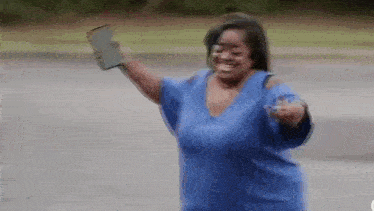 a woman in a blue shirt is holding a purse in her hand and smiling .